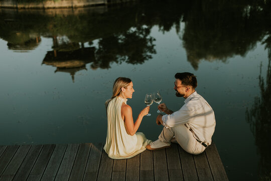 Couple enjoys romantic evening by the serene lake with glasses raised
