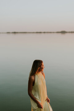 Woman stands by the water while watching the sunset over the horizon