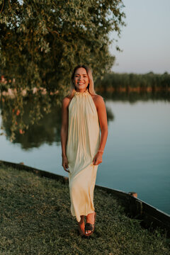 Woman standing by the water in a light dress during sunset near the lake