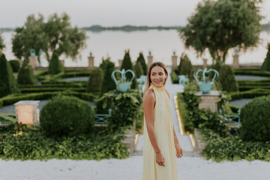 Beautiful young woman in elegant dress enjoys serene garden by the lake