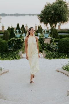 Elegant woman walking in a serene garden at sunset by the water