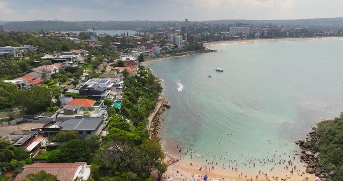 Sydney coastline showcasing modern villas and luxury houses nestled along the picturesque cliffs, with people enjoying the turquoise water and relaxing on Shelly Beach during a sunny summer vacation