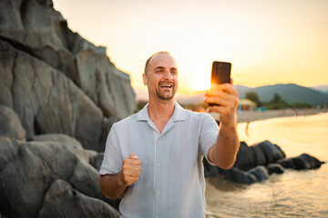 Happy man smiling, taking a selfie on a beach during sunset, enjoying summer vacation © Jelena