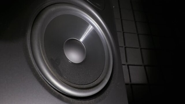 A close-up shows a black subwoofer speaker cone vibrating intensely while playing loud bass music. Concept of high volume audio dynamics, powerful sound waves, and deep frequencies.