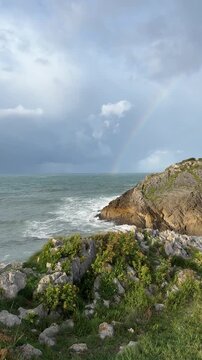 Atlantic coastline after the rain, dramatic sky, gusty wind and a bright rainbow above the ocean.
