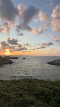 An elevated view of a sheltered Atlantic cove with the iconic sea stacks of Costa Quebrada, gentle waves rolling toward the shore in warm sunset light beneath expressive evening clouds.