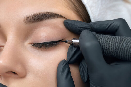 Permanent makeup artist applying eyeliner tattoo on eyelid of young woman. Cosmetologist performing micropigmentation procedure in beauty salon. Professional skin care and aesthetic enhancement.