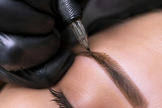 Tattoo artist applying permanent makeup on woman eyebrow. Brow pigmentation procedure with needle device professional tool. Cosmetic beauty treatment for face and skin enhancement.