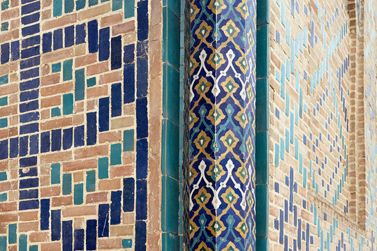 Ornate tilework detail on a column at Bibi Khanum Mosque in Samarkand. Glazed ceramic patterns in blue, gold, and turquoise against brick walls, ideal for travel and heritage publications.
