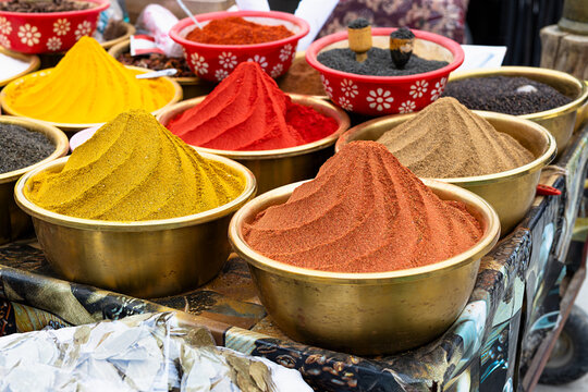 Ground spices displayed in cone-shaped mounds in brass bowls at a traditional bazaar in Bukhara, Uzbekistan. Vibrant yellow turmeric, red paprika, and brown cumin create a colorful arrangement.