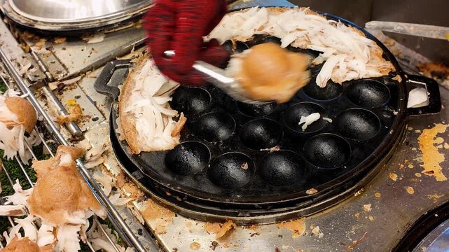 Close-up of a street food vendor removing freshly cooked traditional Thai Khanom Krok coconut pancakes from a cast iron pan at a night market in Phuket, Thailand. Authentic Asian coconut dessert prepa