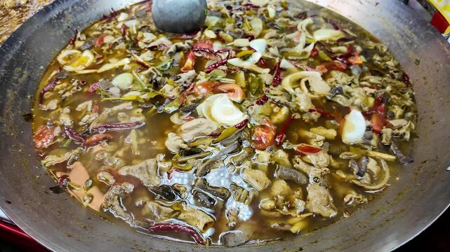 Close-up of a large pan filled with traditional Thai street food stew made with mixed meat, herbs, vegetables and red chili peppers at a local night market in Phuket, Thailand. Authentic Asian cuisine