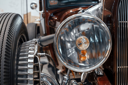 Close-up of a custom hot rod front end featuring a round headlamp, exposed suspension, finned brake drum, and ribbed front tire.