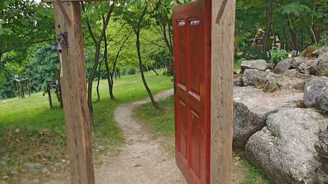 Red wooden door on a rustic structure with a hand pointing toward the handle and entrance detail
