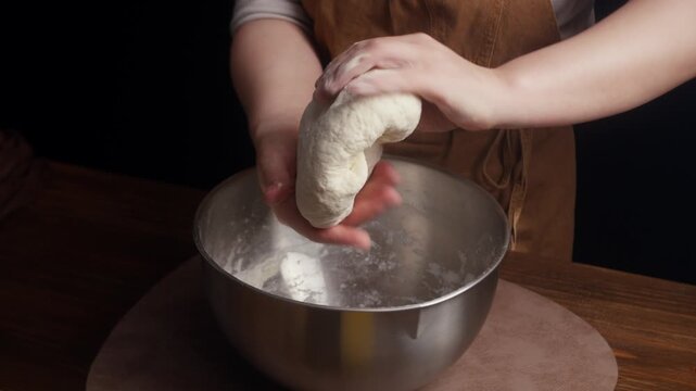 Close up of hands kneading homemade dough in a mixing bowl, then lifting a smooth round dough ball. Traditional bread making process in a rustic home kitchen.