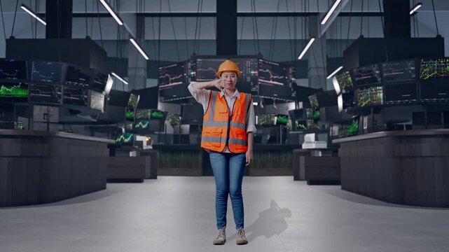Full Body Of Asian Female Engineer With Safety Helmet Showing Thumbs Down Gesture And Shaking Her Head While Standing at Financial Trading Control Room