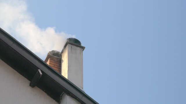 Smoke rising from two house chimneys against blue sky, close-up with copy space