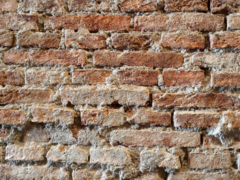 Texture of ancient exposed red brick wall arrangement with rough cement in classic medieval industrial style.
