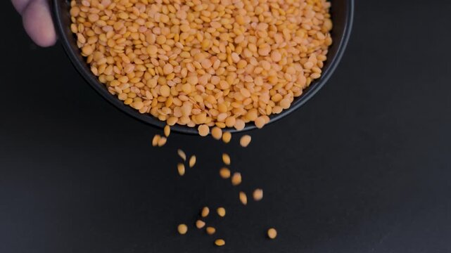 Black bowl pouring orange lentils and leaving frame low key 4k
