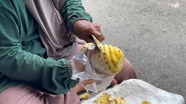 Close-up of skilled hands peeling a fresh pineapple with a traditional knife, creating a clean spiral pattern on the fruit. Tropical fruit preparation, craftsmanship, food processing.