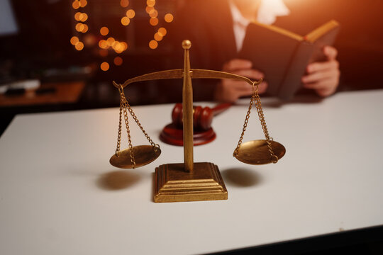 Scales of Justice and Gavel on Desk with Lawyer Reading Law Book in Background