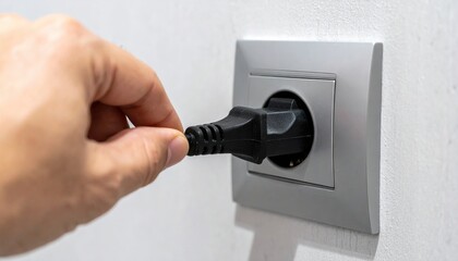 Naklejka premium A close-up shot of a hand pulling a black power cord and plug directly out of a modern electrical wall socket, safety concept.