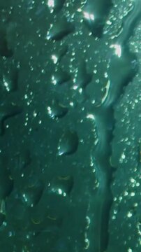 Rain drops on green glass surface. Water droplets sliding down a smooth window pane.