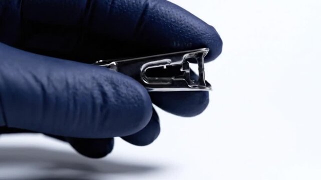 Closeup of a hand in a blue medical glove holding a metal surgical skin staple remover