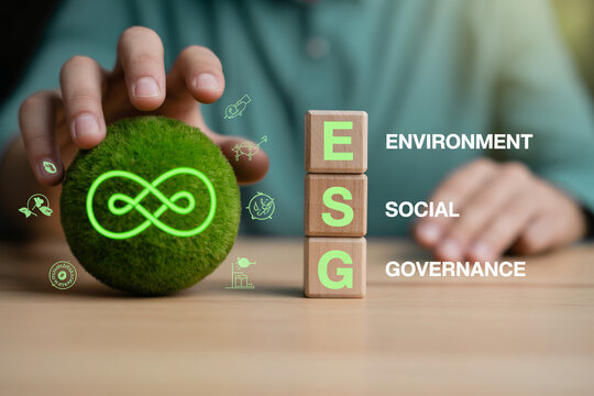 Person touching green sphere with infinity symbol next to wooden blocks with ESG text for sustainability.