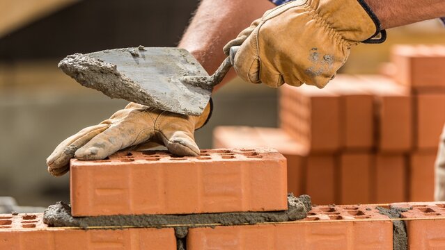 A close-up view of a construction worker using a trowel to apply mortar on a red brick wall project.