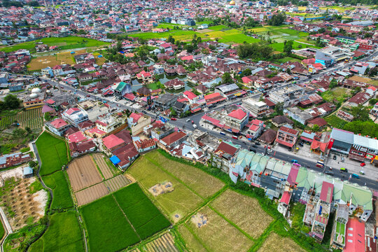 Scenic high-angle landscape of Bukittinggi, Indonesia. The urban cityscape highlights Sudirman street traffic surrounded by densely populated neighborhoods and rice paddies.