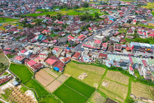 Scenic high-angle landscape of Bukittinggi, Indonesia. The urban cityscape highlights Sudirman street traffic surrounded by densely populated neighborhoods and rice paddies.
