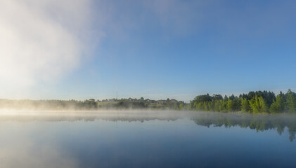 Fototapeta premium Misty Sunrise Over Calm Forest Lake with Village Shoreline, Central Russia