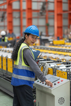 asian female factory supervisor or technician managing in safety vest and hard hat pressing button on the machine control panel to monitor automated production line in industrial manufacturing plant