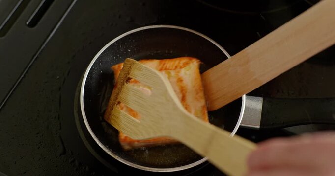 Removing fried salmon fillet from pan using wooden spatulas