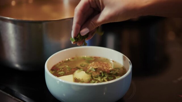 Adding Fresh Green Parsley Herbs Into Bowl Of Hot Homemade Meatball Soup. Cooking Meal