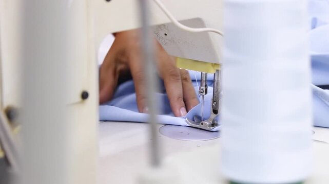 A seamstress's hands are creating a blue fashion garment on a sewing machine inside a textile factory in Neiva, Huila, Colombia. Concept of textile industry and handmade