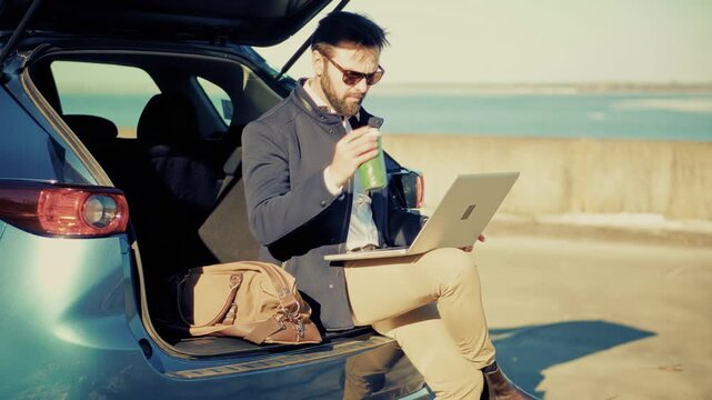Businessman Working On Laptop Sitting In Open Trunk Of Car. Remote Workplace. Freelancer