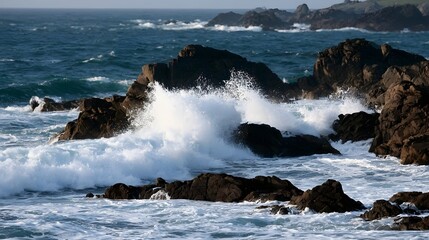 Fototapeta premium Powerful ocean waves crash against dark rocky shores under clear sky creating white foam and dynamic sea spray