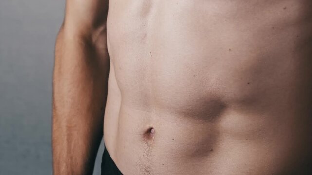 Frontal close-up of a shirtless mans defined torso and abs. He uses both hands to stretch a black resistance band performing a dynamic chest exercise to build strength.