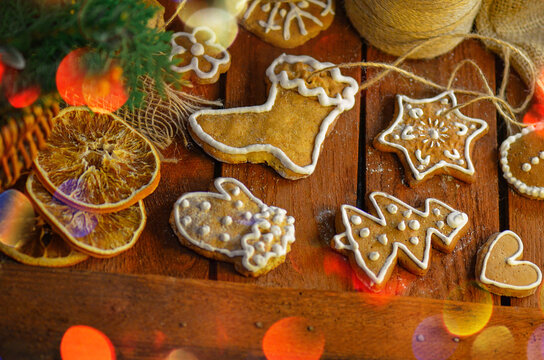 Various decorated gingerbread cookies are arranged across rustic painted wooden planks. Warm tones highlight textured details.