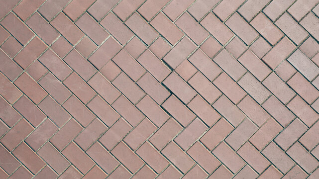 Red brick pavement in herringbone pattern. Textured stone walkway background.