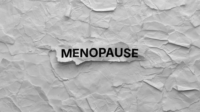 Crumpled piece of paper with word Menopause on torn crumpled white paper pieces background.