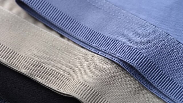 A close-up of elastic waistbands in black, beige, and blue on mens jersey underwear garments.