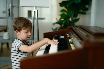 Son little boy education sat diligently practicing the piano in his home small fingertips carefully pressed keyboard keys weaving together melodies even though music today was not yet perfect. © ฺฺฺBoonterm
