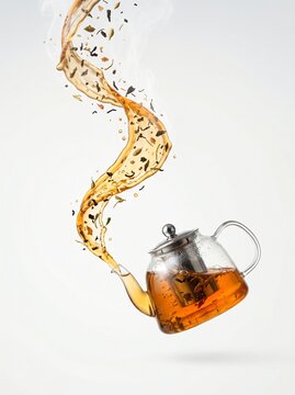 A clear glass teapot pouring hot amber tea that flows upwards instead of downwards,