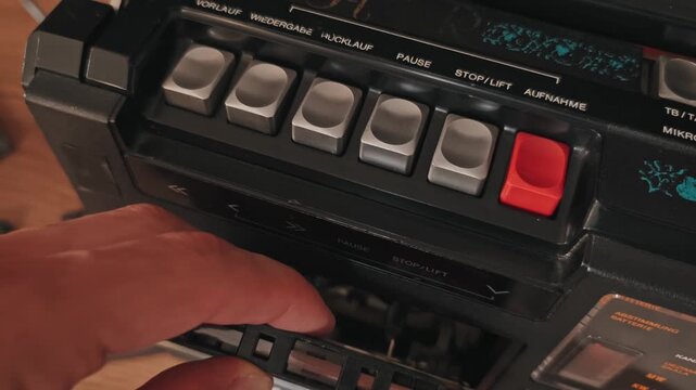 A hand presses the eject button on a retro player to remove and insert an old audio tape. Concept of nostalgia for analog technology, vintage music formats, and eighties electronics.
