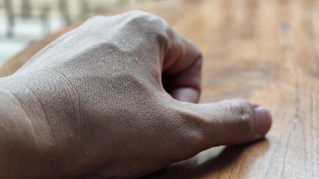 Slow motion macro shot of a human hand tightening into a strong fist then slowly relaxing open on a wooden table, symbolizing anger or control.

