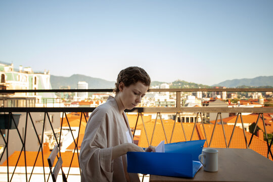 woman in cancer recovery reviews medical documents in a blue folder on a sunny terrace, organizing treatment records, insurance papers and follow up care while traveling
