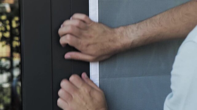 Person adjusting a mosquito screen on hook and loop tape on a window frame, illustrating home maintenance and practical DIY work.